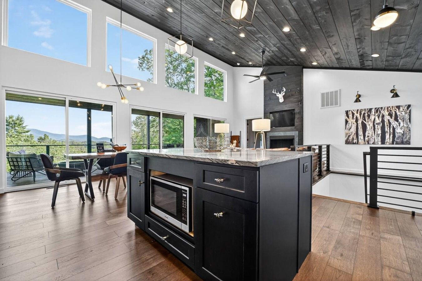 A modern kitchen with a large island, black cabinetry, and a dining area with a view.