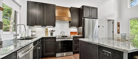 A modern kitchen with dark cabinetry, stainless steel appliances, and a wooden floor.