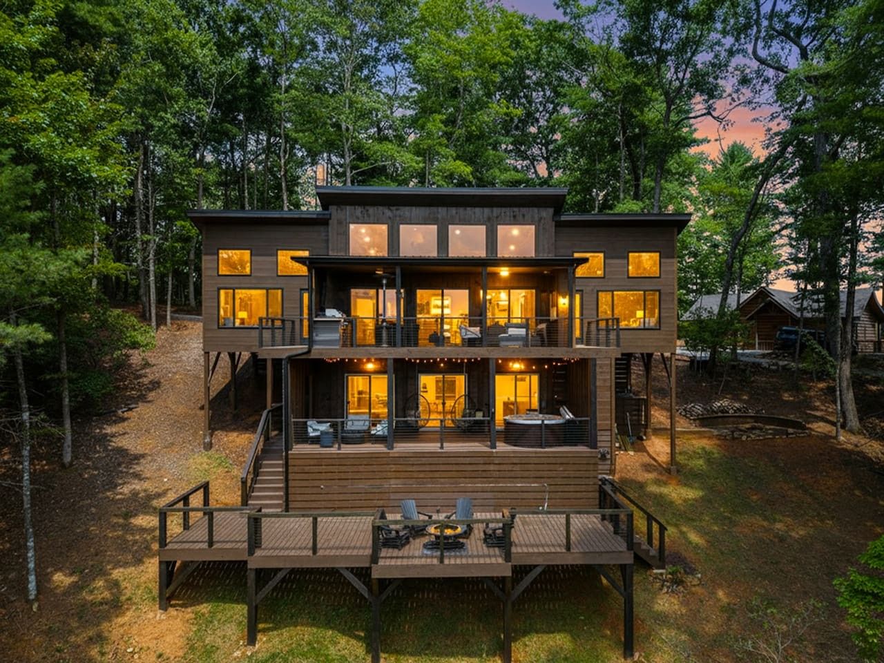 A multi-level wooden cabin with a deck, surrounded by trees.