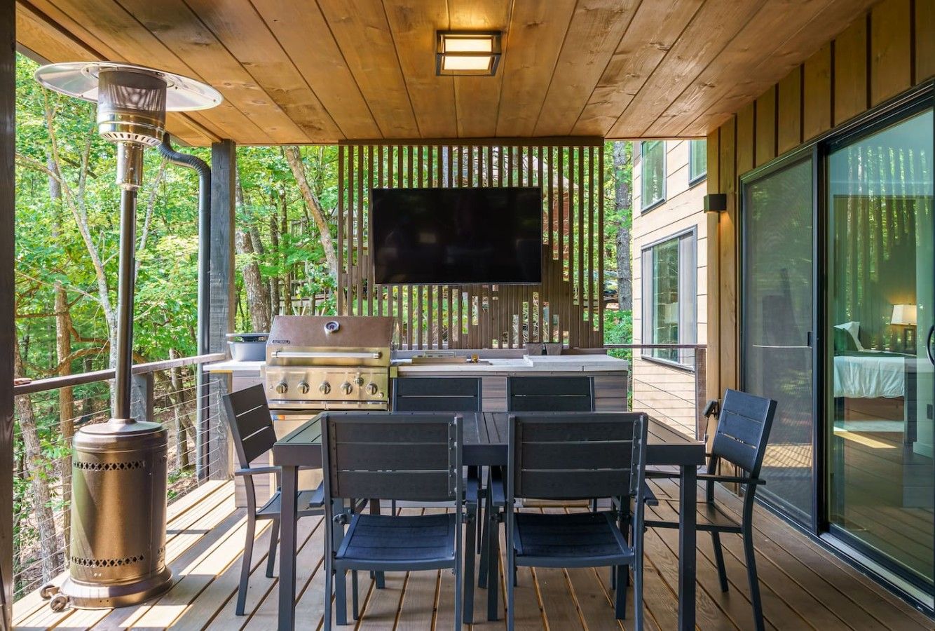 An outdoor deck with a grill, chairs, and a TV screen.