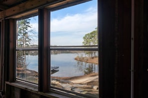 A room with a large window overlooking a calm lake and a dock.