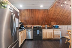 A kitchen with wooden paneling, stainless steel appliances, and a dark wooden floor.