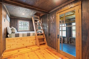 A wooden interior with a bunk bed, a ladder, and a door leading outside.