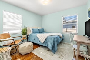 A bedroom with a bed, a chair, a table, and a television.