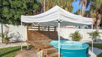 Une terrasse en bois couverte, avec une piscine et une tente blanche.