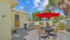 Un patio con una mesa, sillas, un paraguas rojo y una cerca blanca.