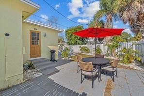 A patio with a table and chairs, a red umbrella, and a white fence.