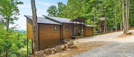 A cabin with a gravel driveway, surrounded by trees.