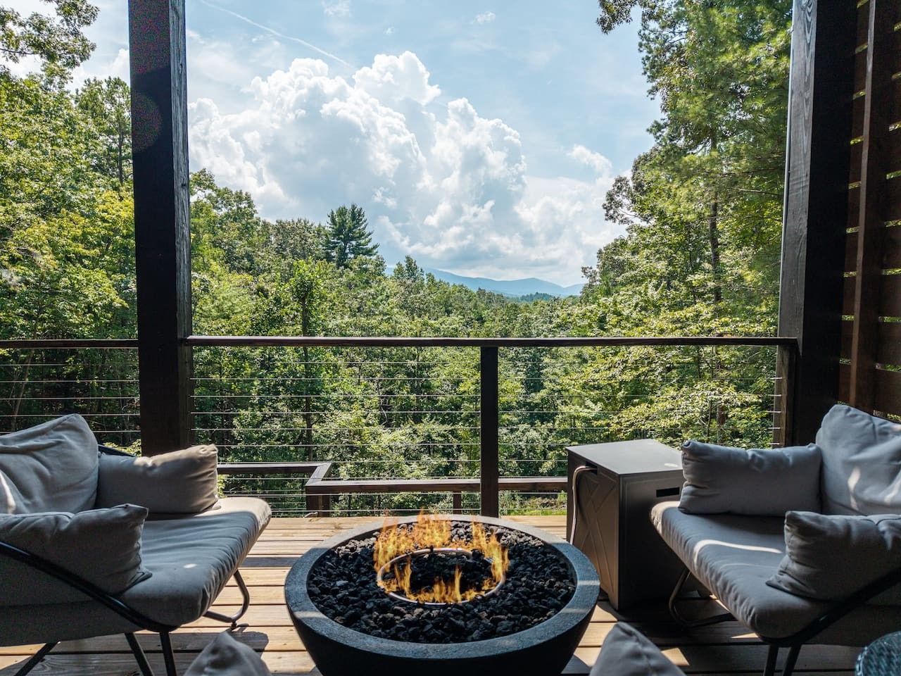 A deck with a fire pit, two sofas, and a view of a forested landscape.