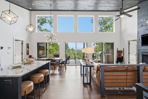 A modern kitchen with a large island, bar stools, and a dining area with a view of the outdoors. - Mountain Haus | 4BR | 3 Decks | Views | Fireplaces (Blue Ridge)