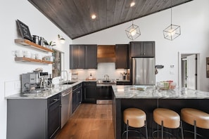 A modern kitchen with dark cabinets, a stainless steel refrigerator, and a marble countertop. - Mountain Haus | 4BR | 3 Decks | Views | Fireplaces (Blue Ridge)