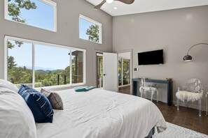 A bedroom with a large bed, a desk, a chair, a TV, and a balcony with a view. - Mountain Haus | 4BR | 3 Decks | Views | Fireplaces (Blue Ridge)