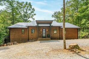 A wooden cabin with a gravel driveway and a metal roof, surrounded by trees. - Mountain Haus | 4BR | 3 Decks | Views | Fireplaces (Blue Ridge)