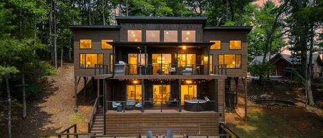 A multi-level wooden cabin with outdoor seating and a deck, surrounded by trees.