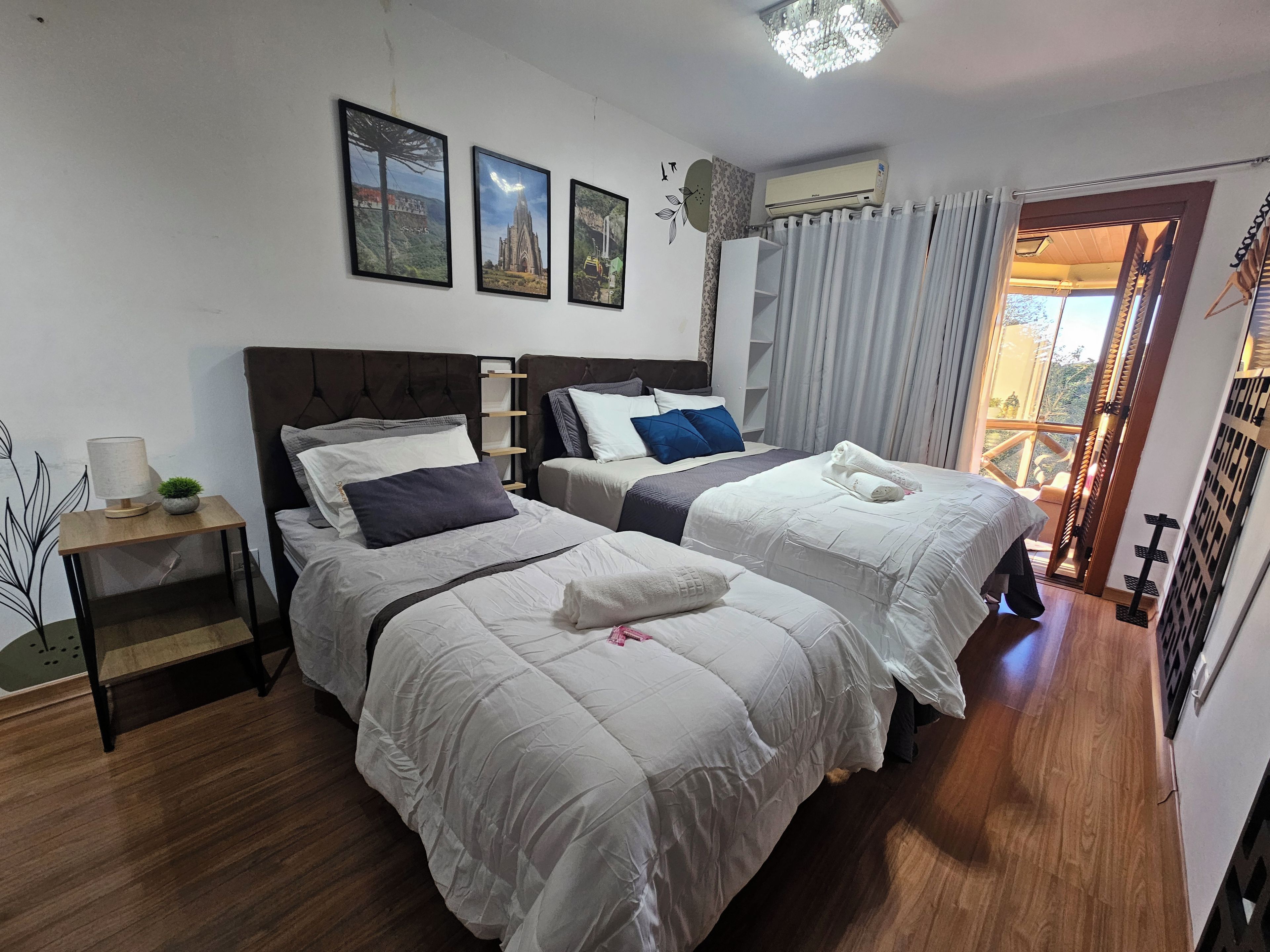 Une chambre d’hôtel avec deux lits, une table de chevet avec une lampe, un climatiseur fixé au mur et une fenêtre avec des rideaux.