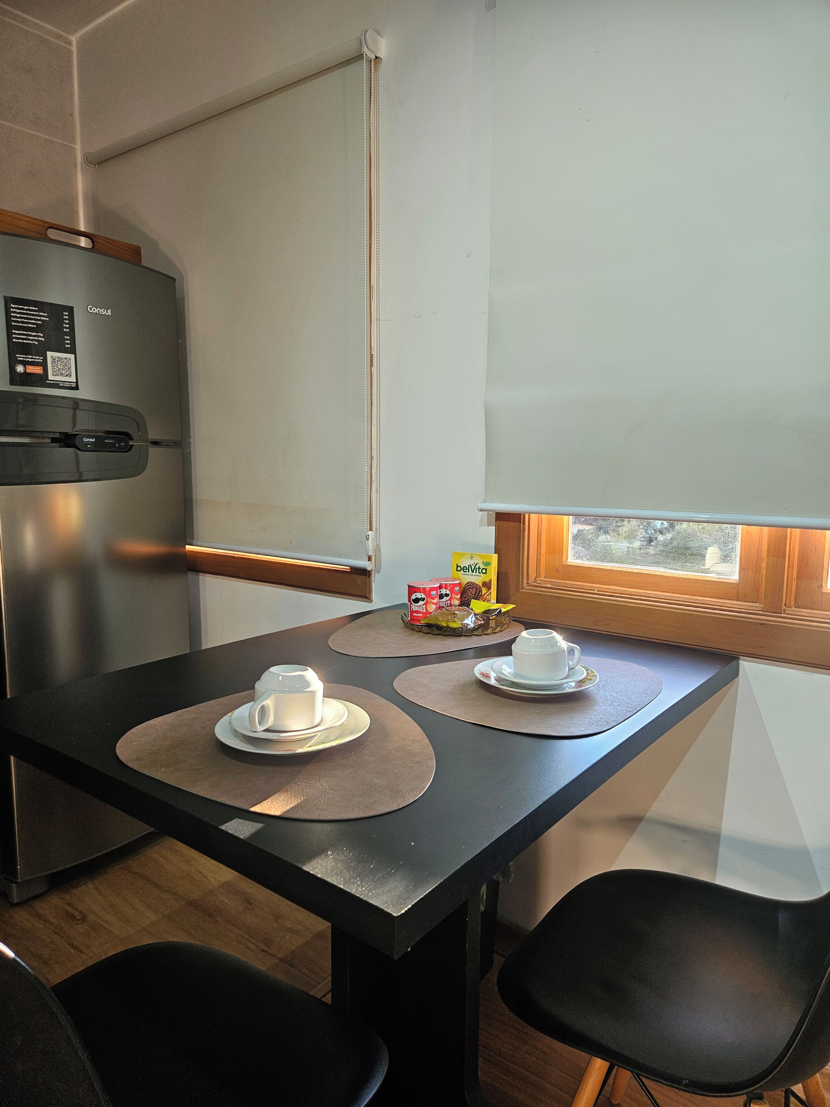 A compact kitchenette with a refrigerator, a small table with two chairs, and a window with a view.