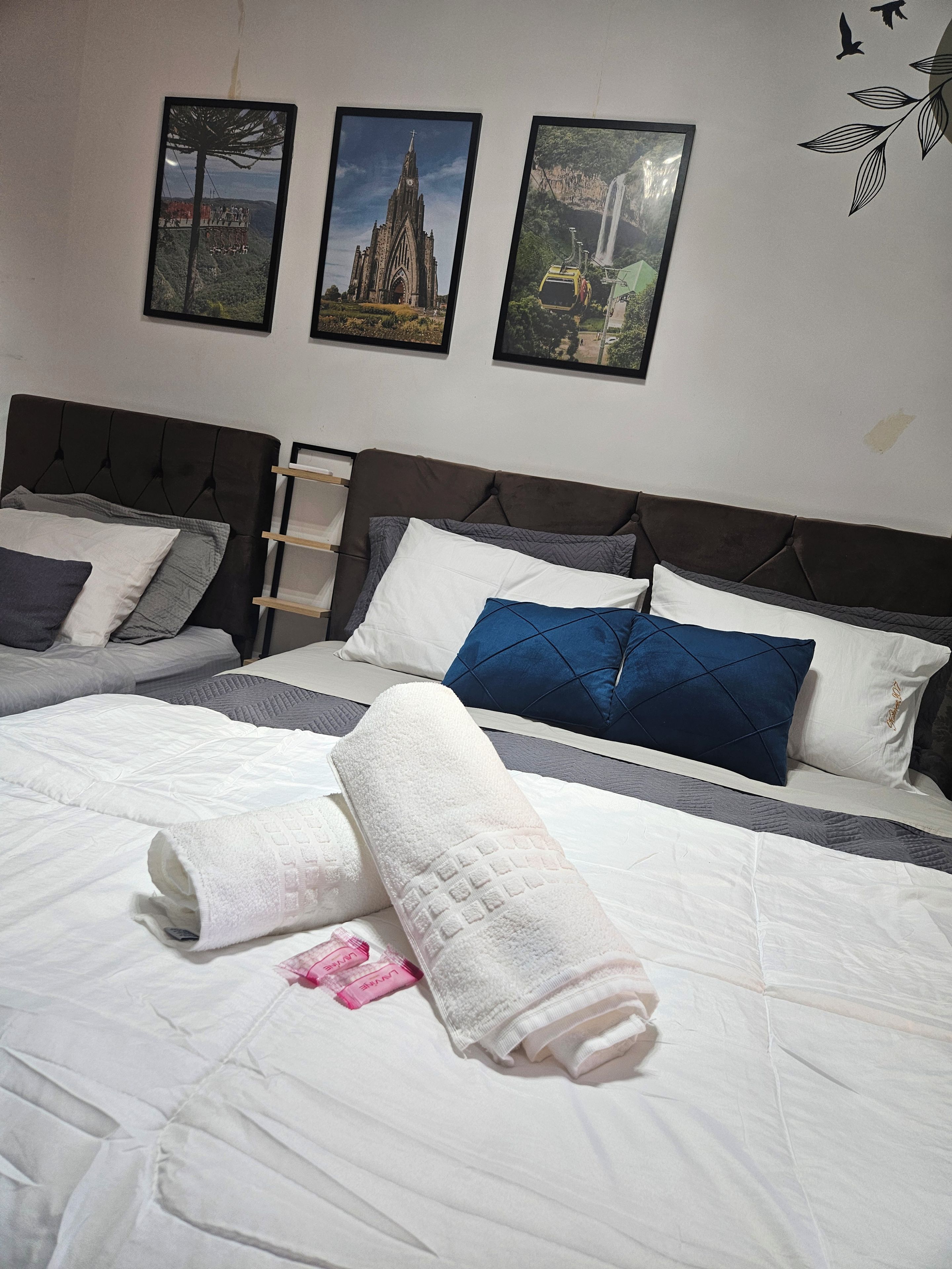 A hotel room with two beds, a nightstand, and three framed pictures on the wall.