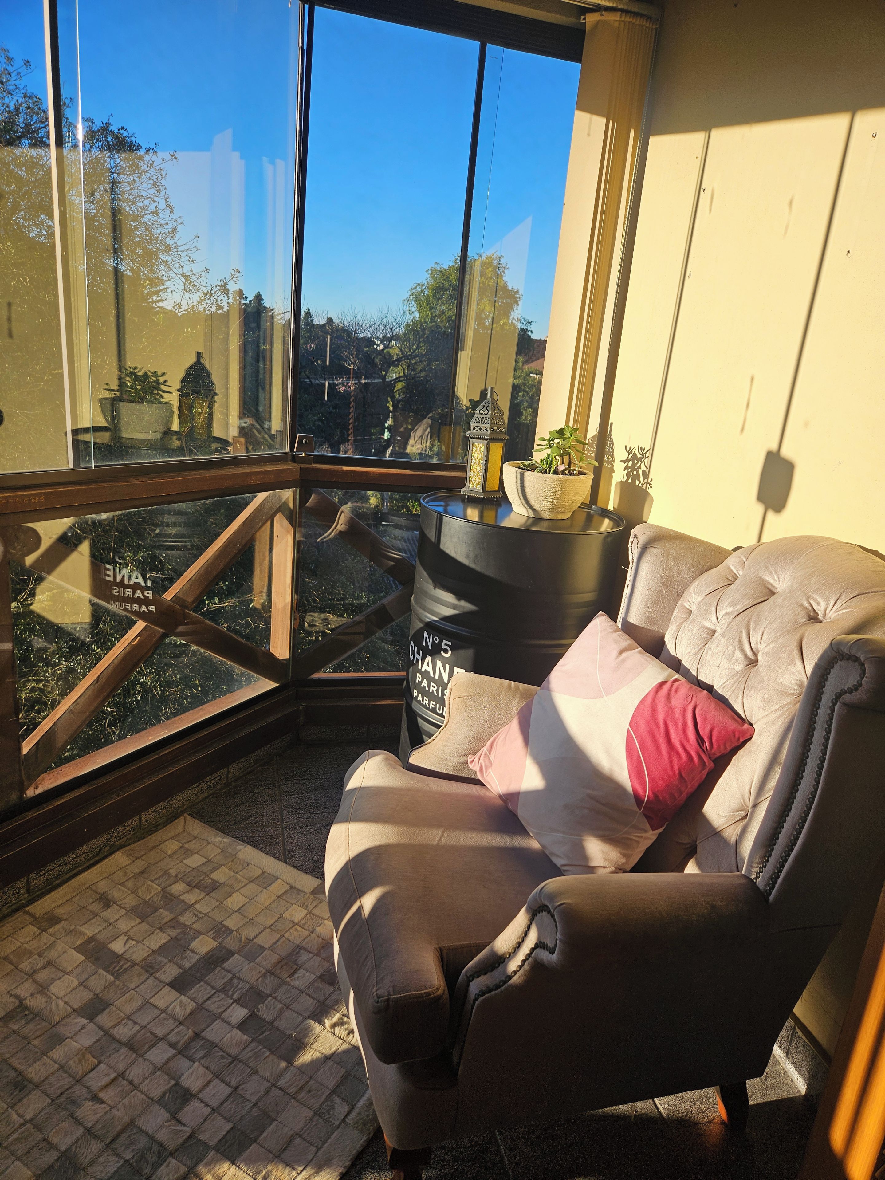 Une pièce d’angle avec un fauteuil confortable, une petite table sur laquelle est posée une plante en pot, et une vue dégagée par une grande fenêtre.