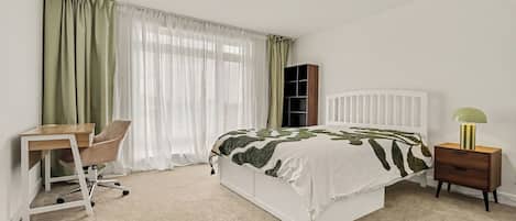 A bedroom with a bed, a desk, a chair, a nightstand, and a lamp.