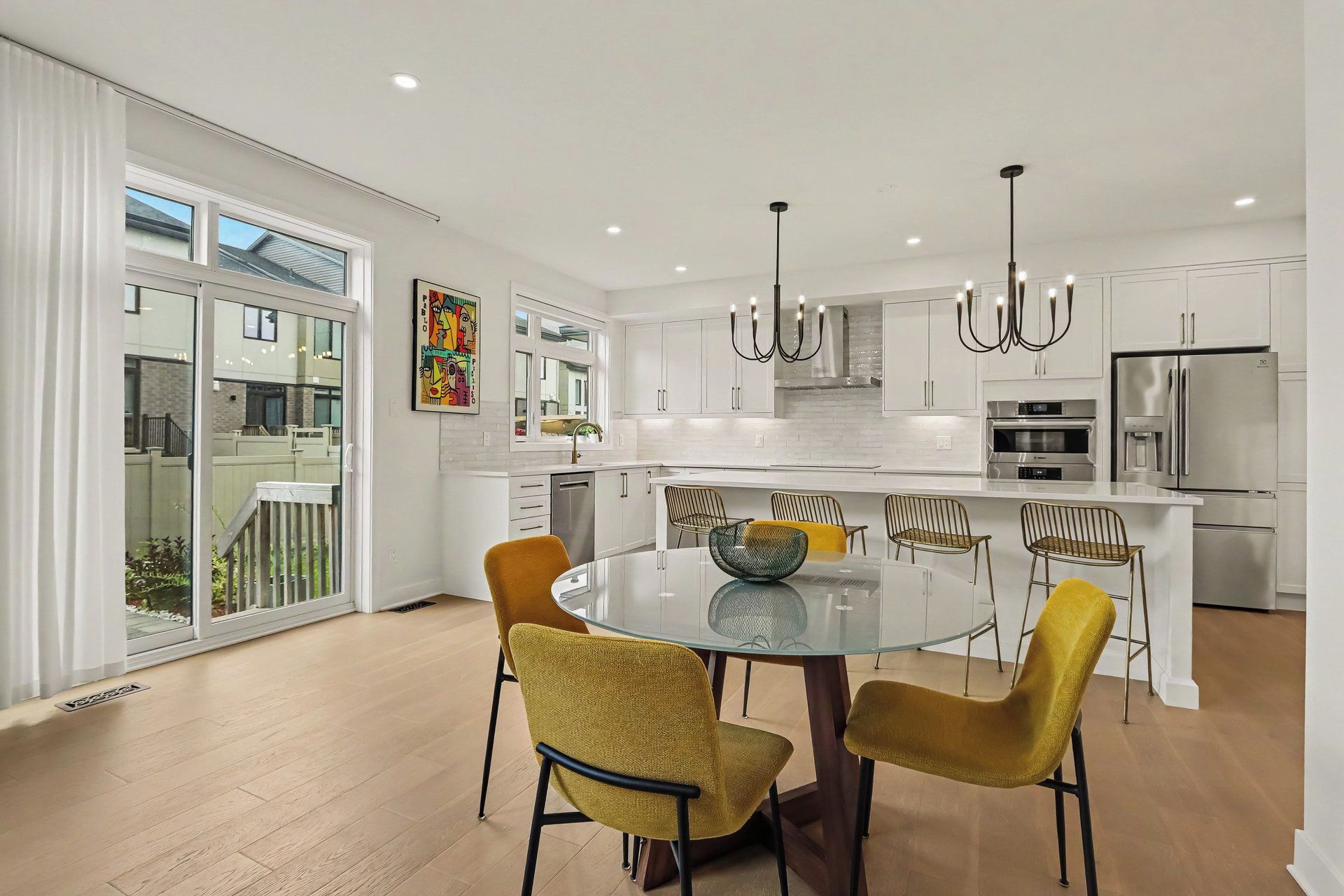 A modern kitchen with white cabinetry, stainless steel appliances, and a round glass dining table with four chairs.
