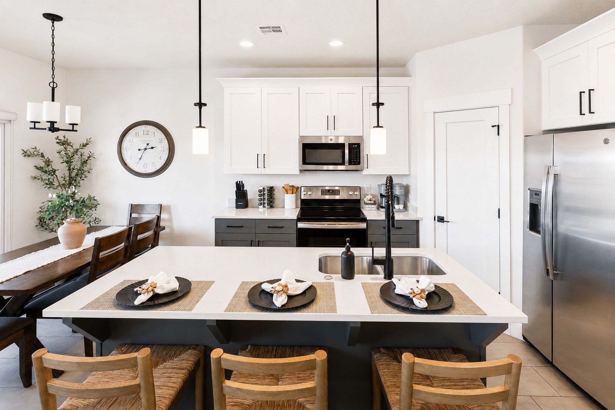 A modern kitchen with white cabinetry, stainless steel appliances, a central island with seating, and a dining area with wooden chairs.
