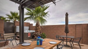 Un patio esterno con tavolo in legno, sedie, barbecue e una palma.