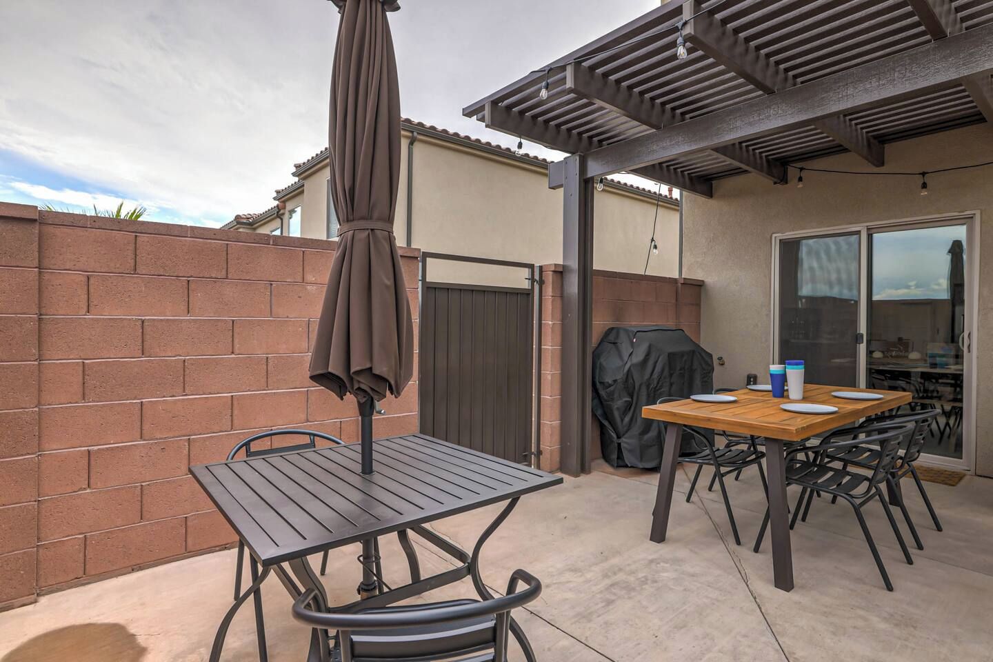 Un espacio al aire libre con patio, una mesa, sillas, una sombrilla y una parrilla.