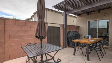 Zona de pati exterior amb taula i cadires, una ombreig cobert i una barbacoa.