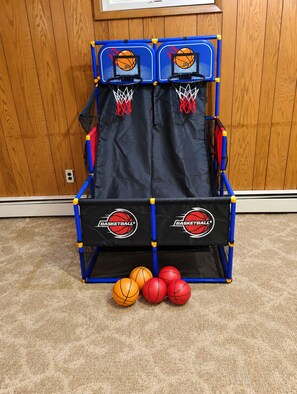 En flytbar basketballkurv med to backboards, et net og et sort banner med ordet 'BASKETBALL' på. Der er tre basketballs foran kurven.