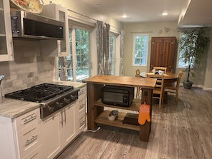 A kitchen with a stove, microwave, and wooden table with chairs. - Beautiful Private Forest Getaway in Peachtree Corners. (Peachtree Corners)
