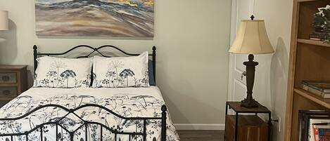 A bedroom with a bed, a painting, a lamp, and a bookshelf.