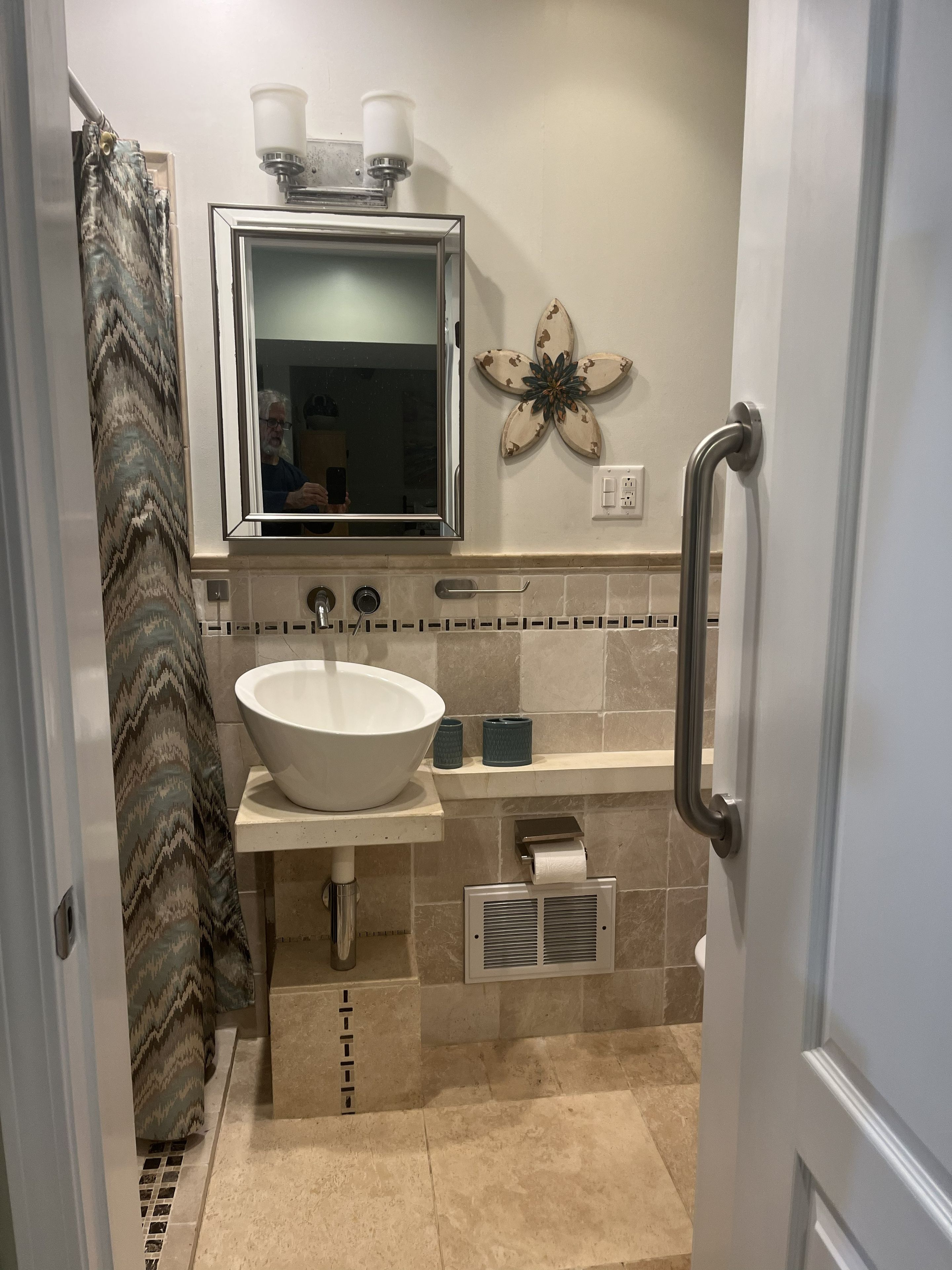 A bathroom with a large white sink, a mirror, a towel dispenser, and a shower curtain.