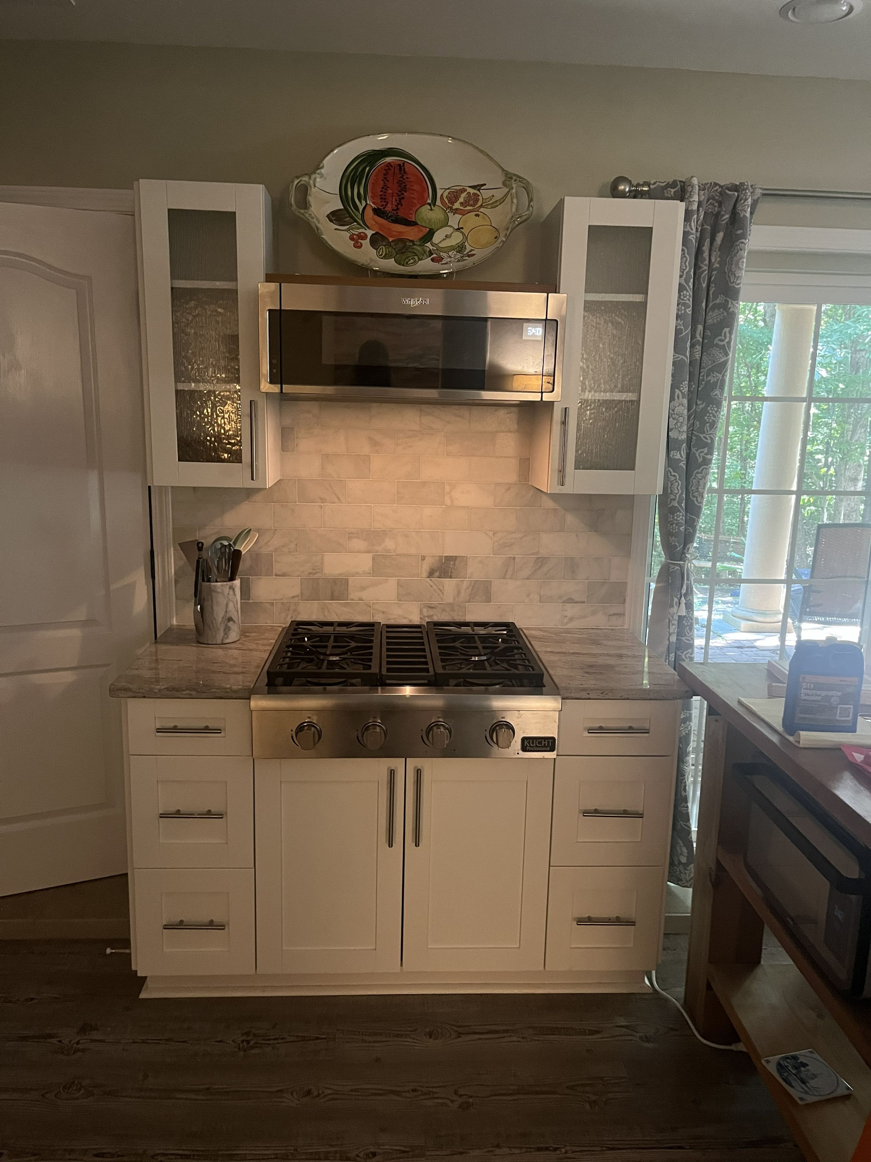 A kitchen with white cabinets, a stainless steel range, and a decorative fruit plate above the microwave.