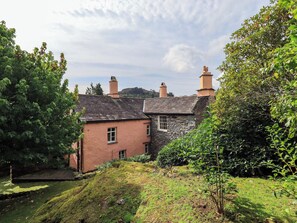 A stone house with a sloped roof, surrounded by lush greenery and a small water feature. - Hart Head Farm (Ambleside)