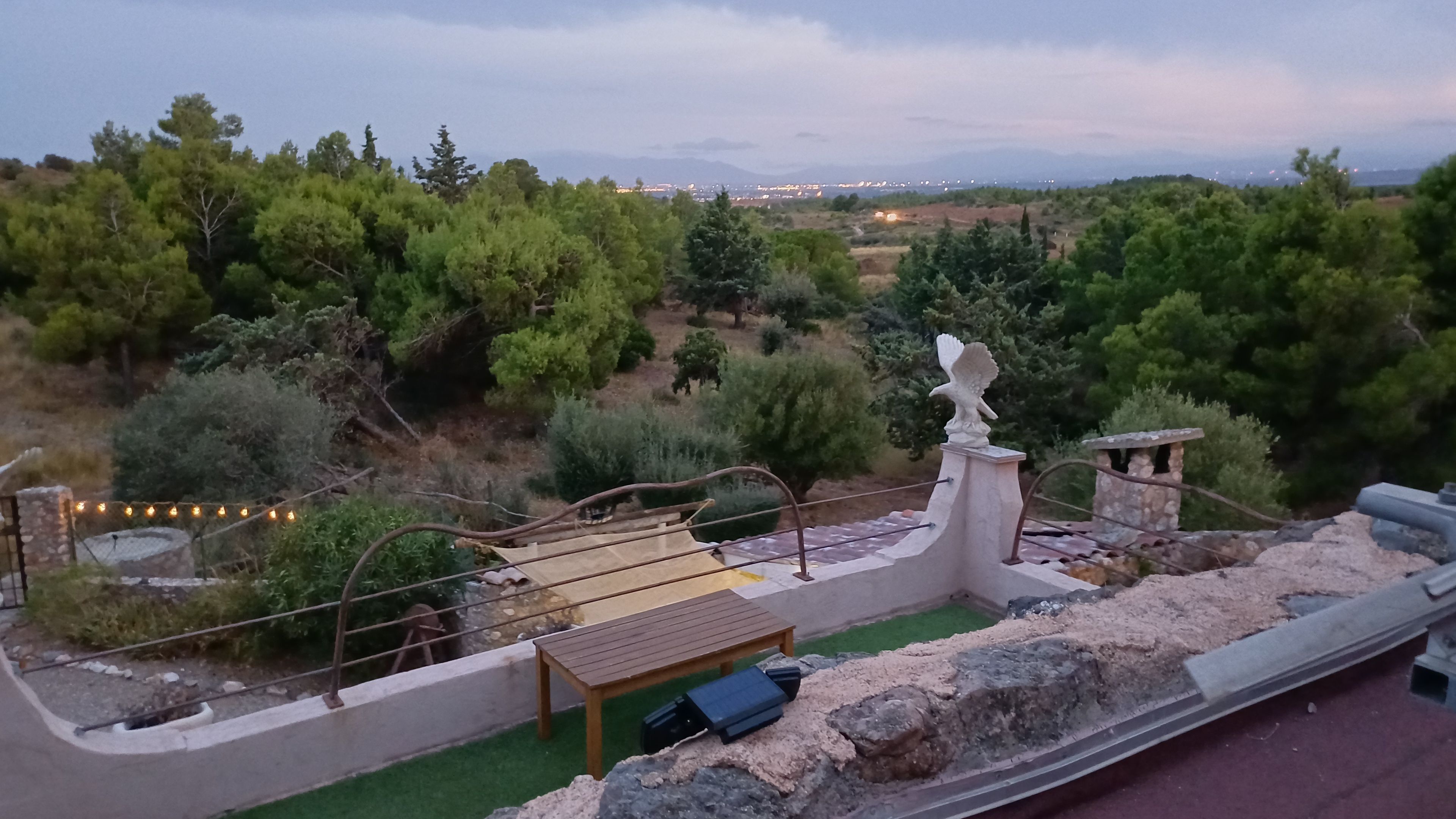 Eine Terrasse mit Steinbalustrade, einem Holztisch und einer Adlerstatue.