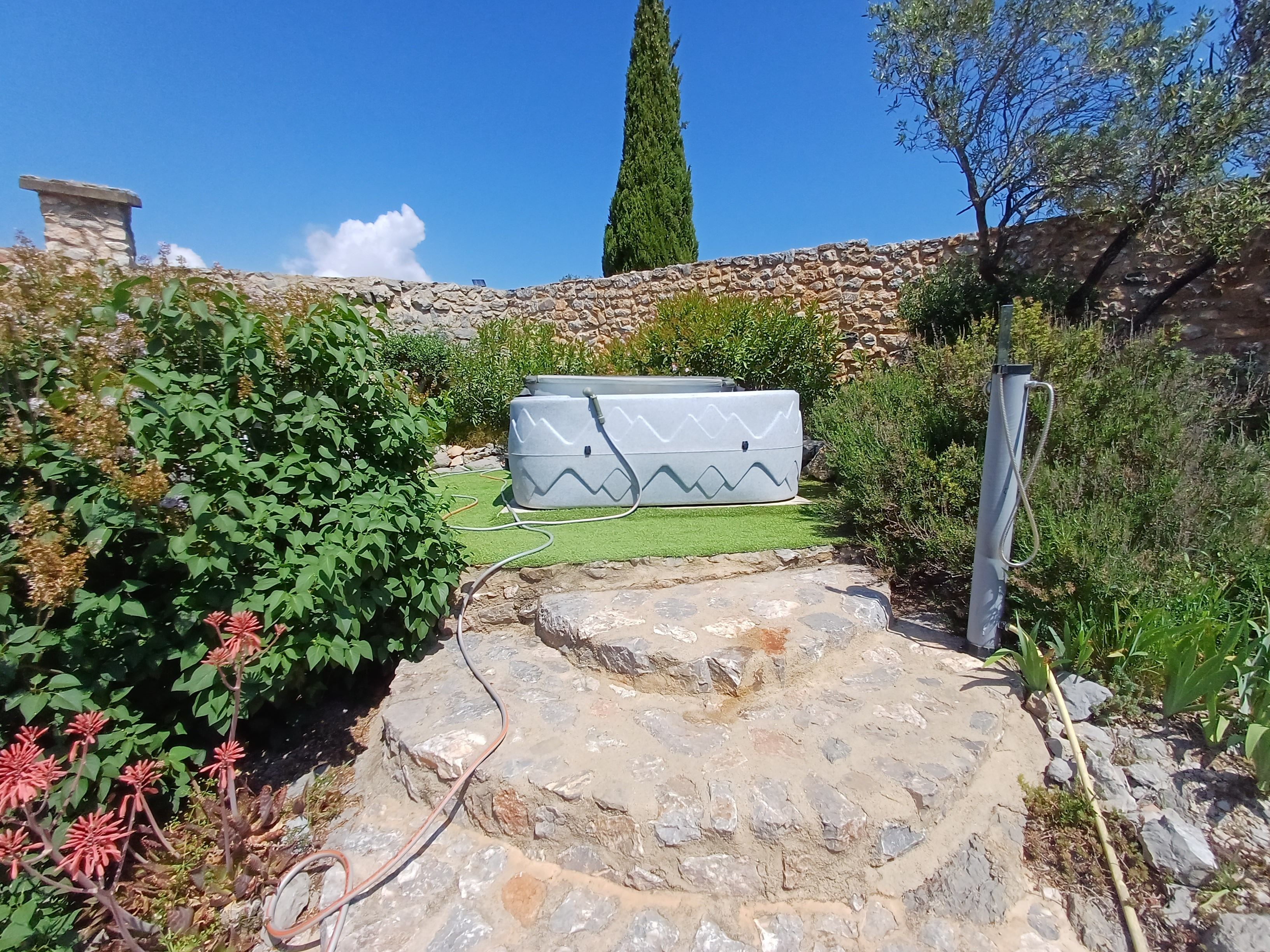 A stone pathway leading to a building with a stone wall and a tall tree.