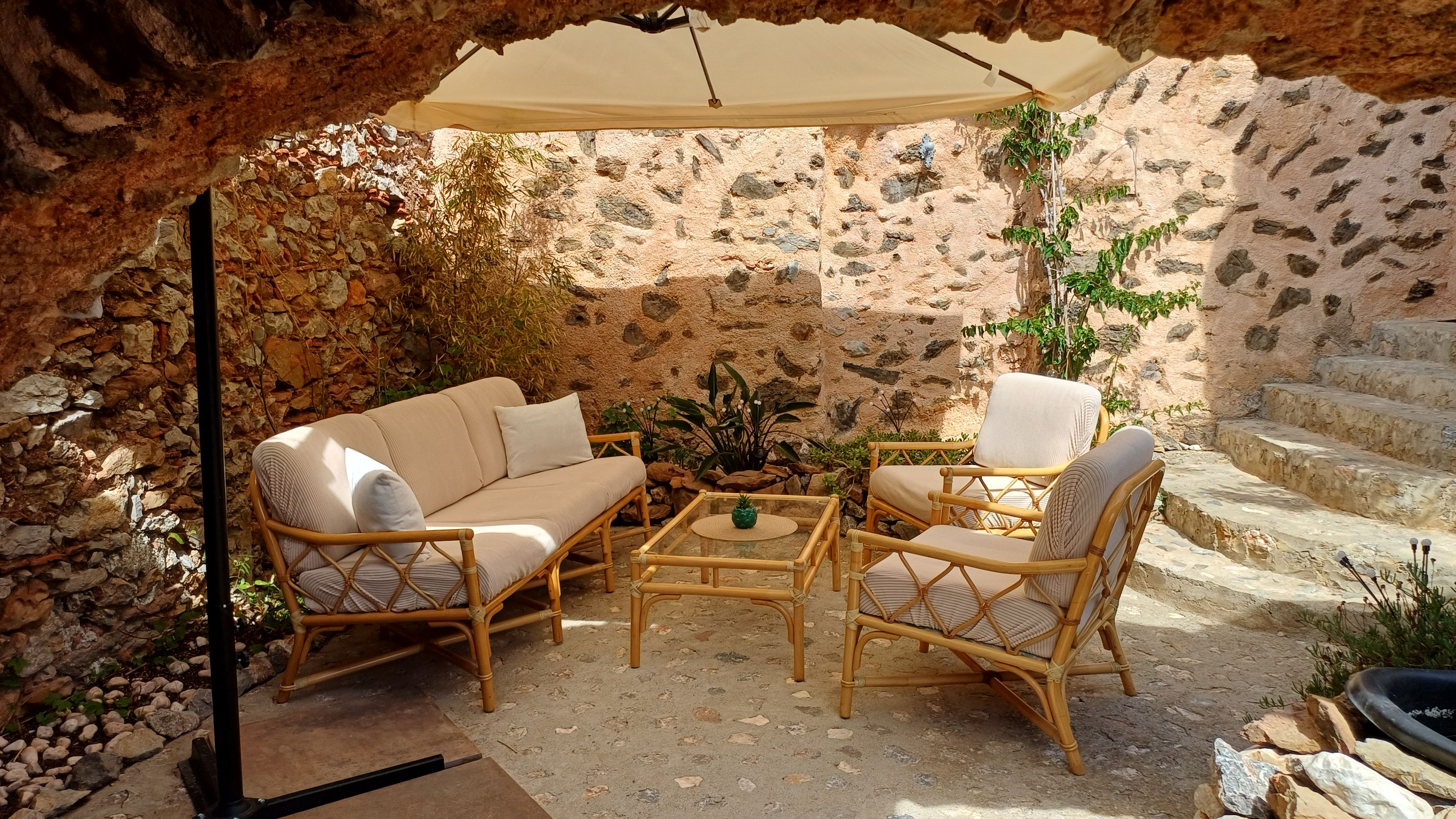 An outdoor seating area with wicker furniture, a stone wall backdrop, and a canopy providing shade.