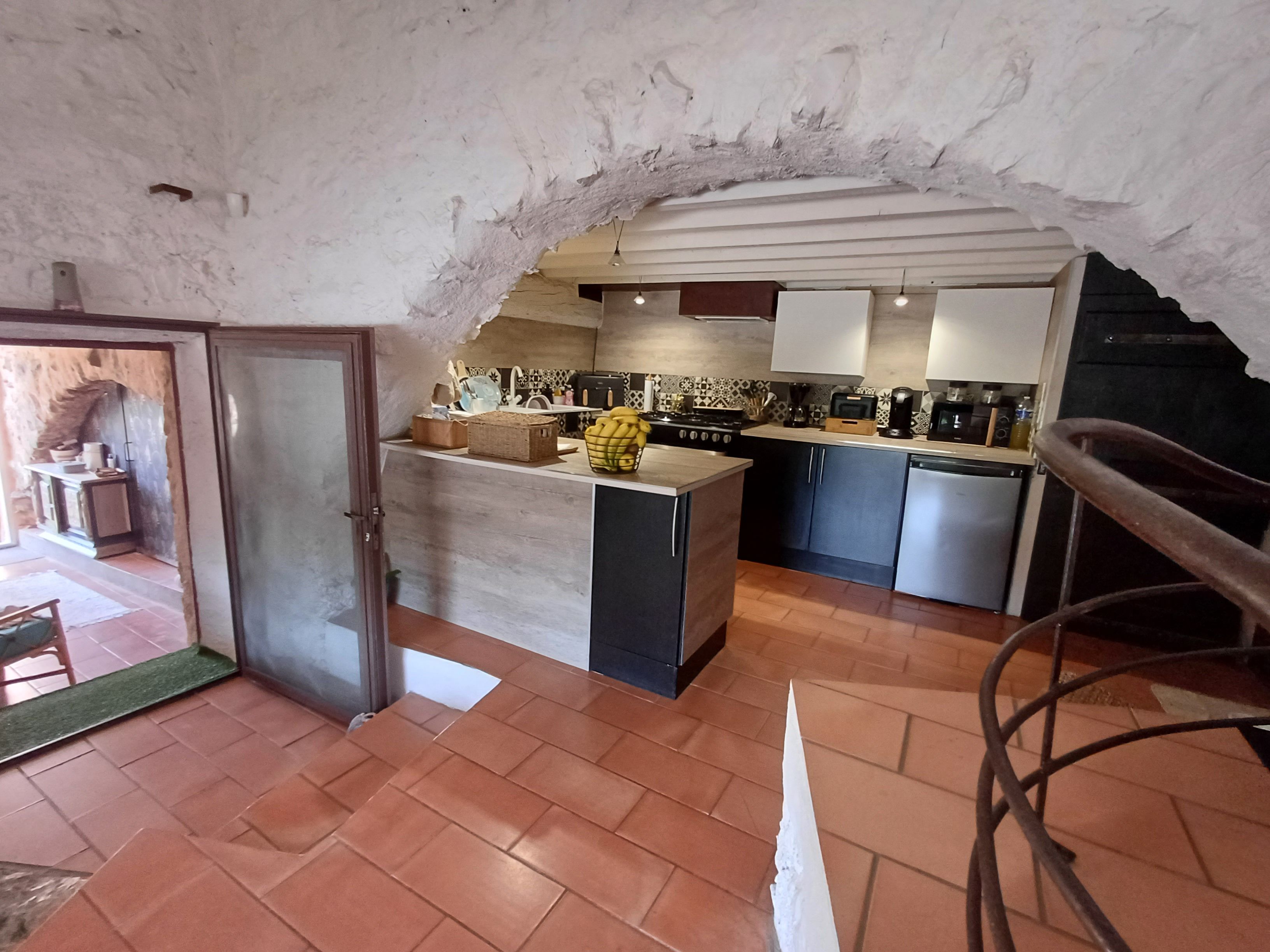A kitchen with a rustic stone ceiling, a central island with a sink, and a stove.