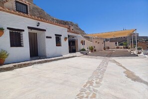A courtyard with a white building, a stone pathway, and a covered area.