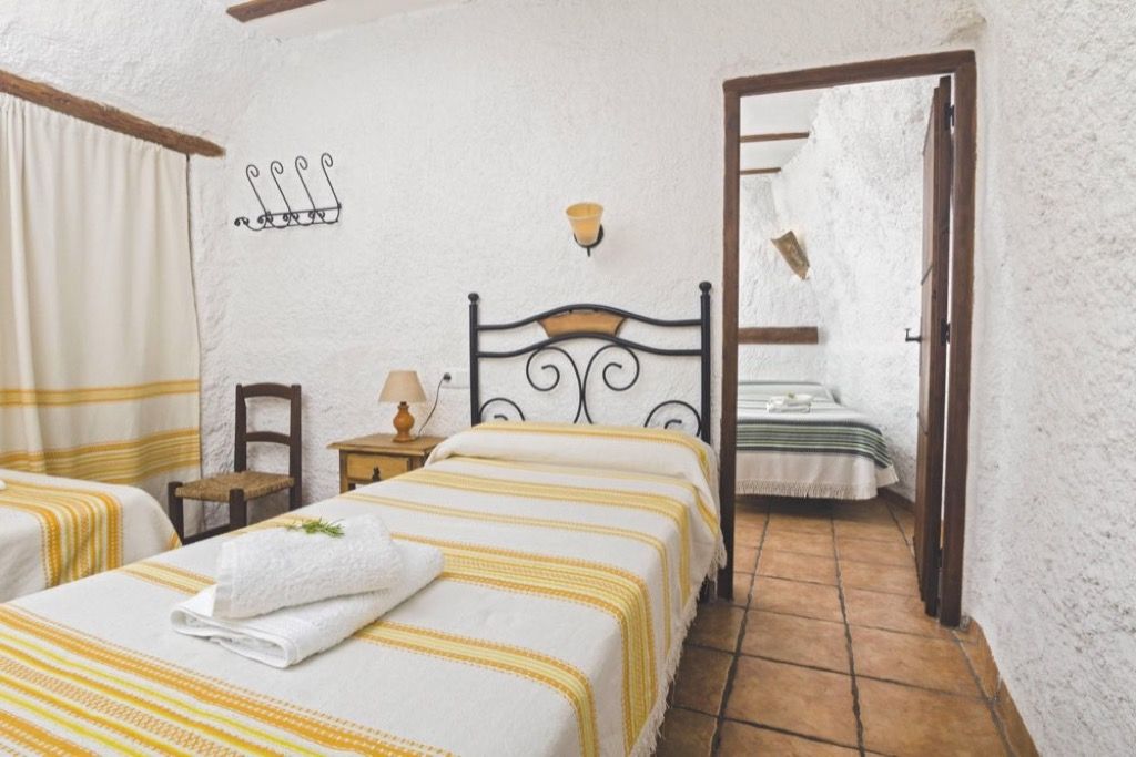 A bedroom with two beds, a wooden headboard, a small bedside table with a lamp, and a wall-mounted light fixture.