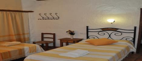 A room with two beds, a nightstand, a chair, and a wall-mounted light fixture.