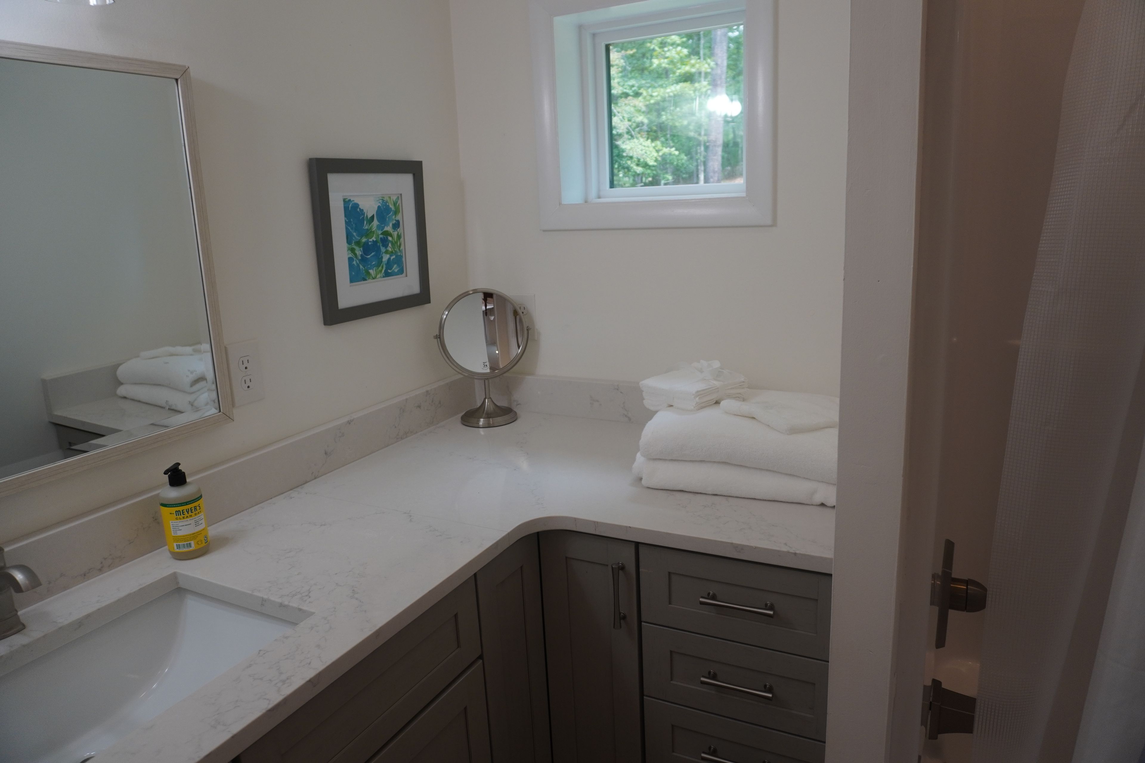A bathroom with a sink, mirror, and window. There are towels stacked on the counter.