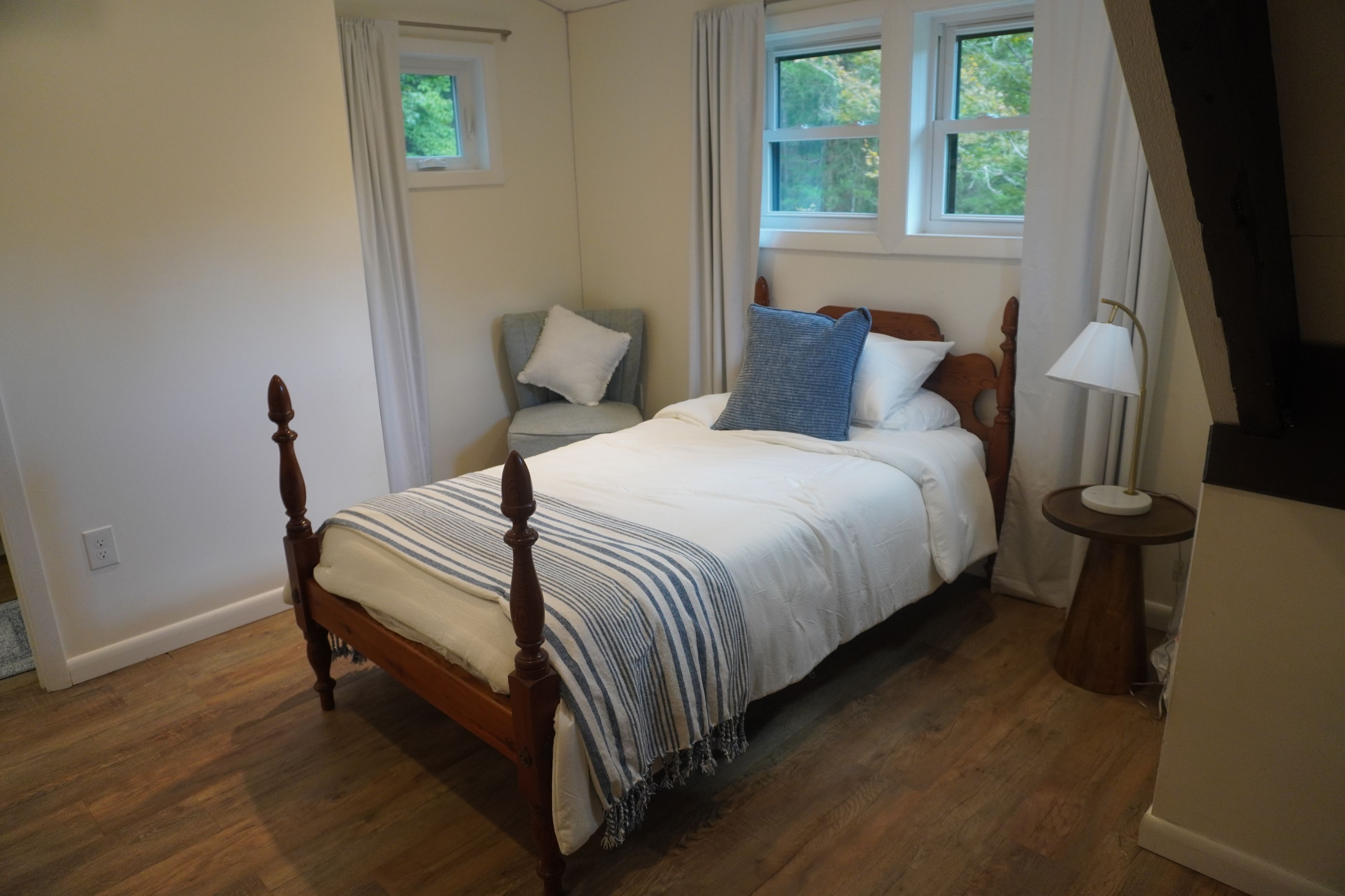 A bedroom with a four-poster bed, a nightstand, a lamp, and a window with curtains.