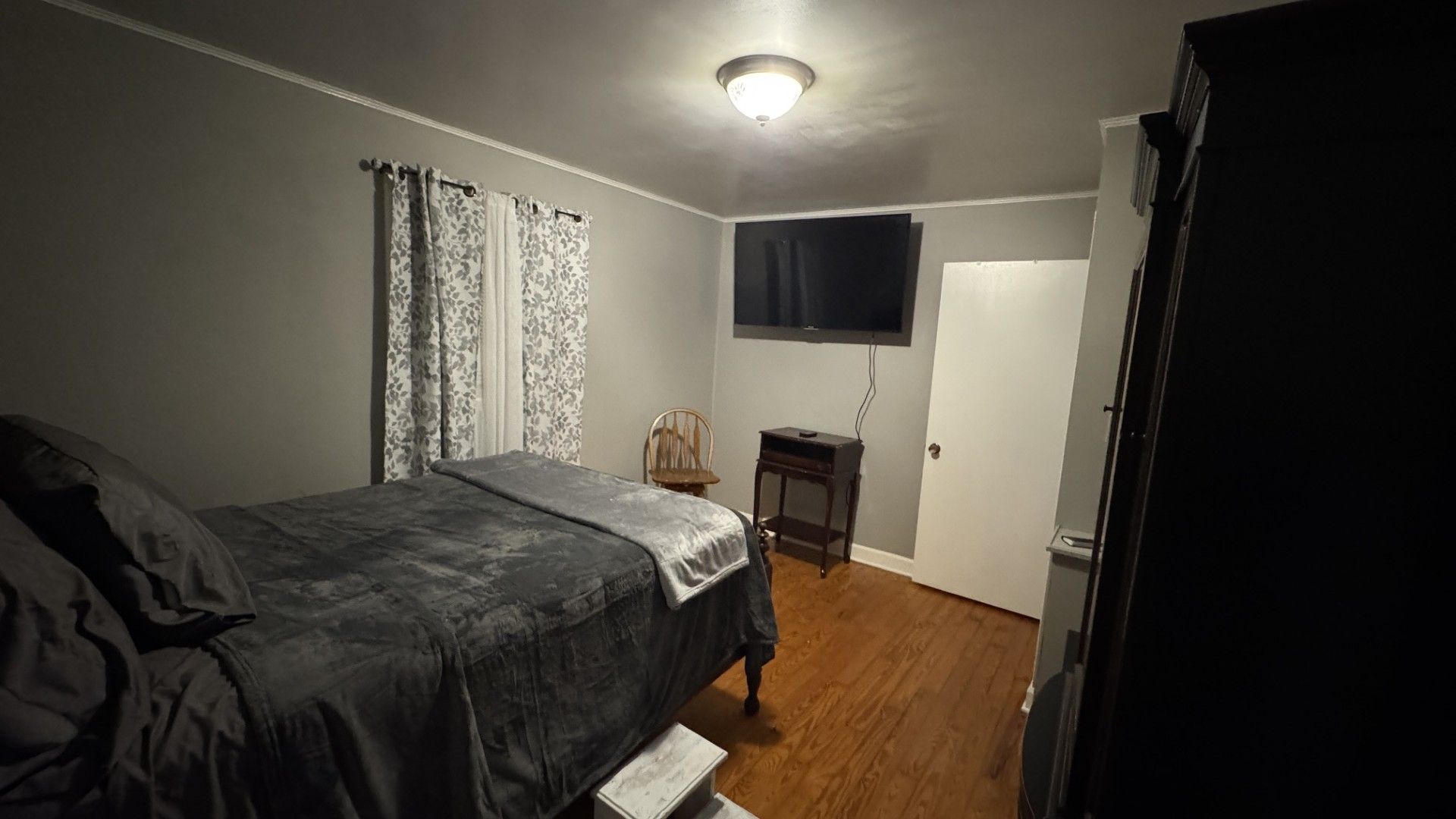 A bedroom with a bed, a television mounted on the wall, and a door.