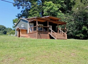 Eine Holzhütte mit Veranda und Treppe, umgeben von einer grünen Wiese und Bäumen.