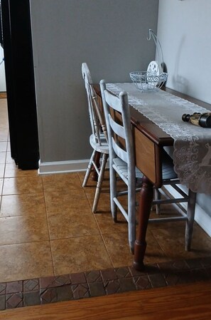 A dining table with a lace tablecloth, a metal bowl, and a bottle on it. - The Green House                                Statesville,NC (Statesville)