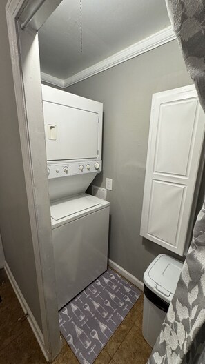 A compact laundry room with a washing machine, dryer, and a small trash bin. - The Green House                                Statesville,NC (Statesville)