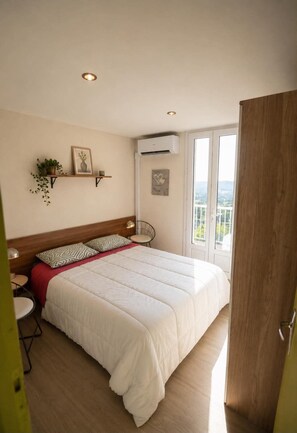 A bedroom with a large bed, a bedside table, a chair, a shelf with plants, and a window with a view. - BELLEVUE VILLA, Pool - Air Conditioning - Panoramic View - Pets Welcome (Ayen)