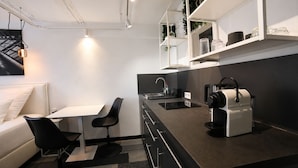 Et moderne køkken med en sort bordplade, hvide skabe, en kaffemaskine og et spiseområde med et hvidt bord og sorte stole.