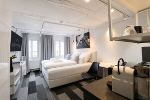 Habitación de hotel con cama, escritorio, silla, zona de cocina y un ventanal grande.